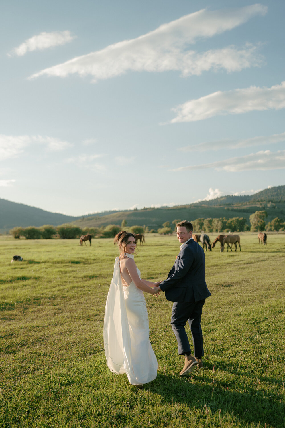 Bride and groom walking hand-in-hand with majestic Teton Mountains  in the background for a French blue summer wedding in Jackson, WY.