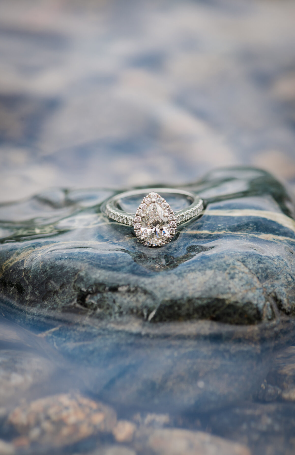 Photos on a beautiful engagement ring sitting on a rock and getting the lake water around the ring.