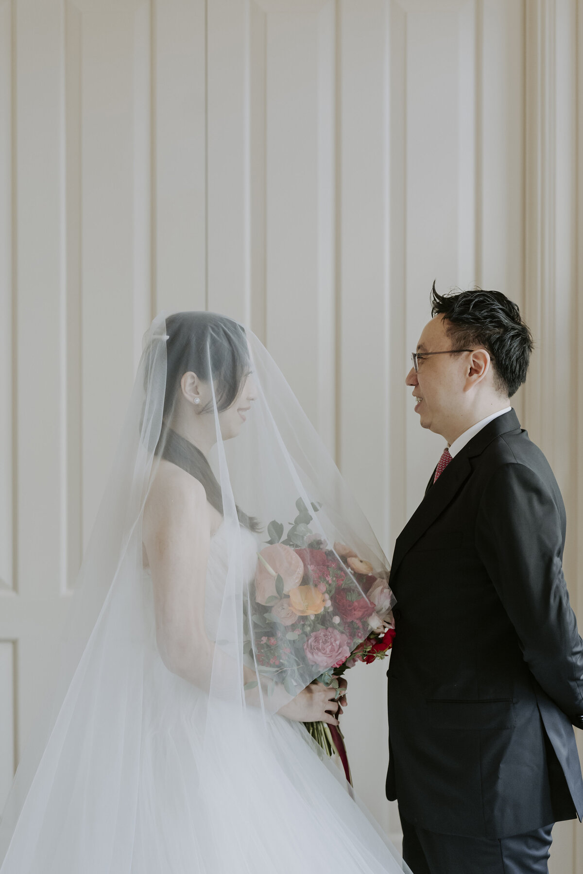 bride holding flowers and groom lifting her veil in Singapore