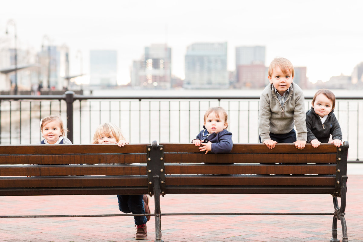 five toddlers sitting on a bench and peeking over the top in Boston Seaport