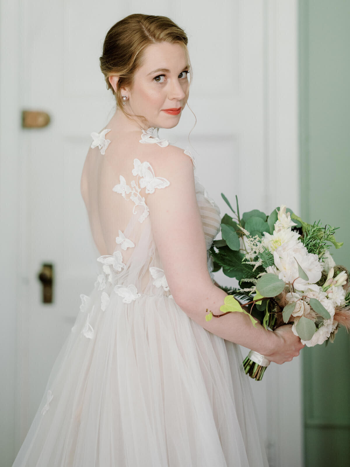 The bride is holding her flower bouquet while looking sideways, with her back showing