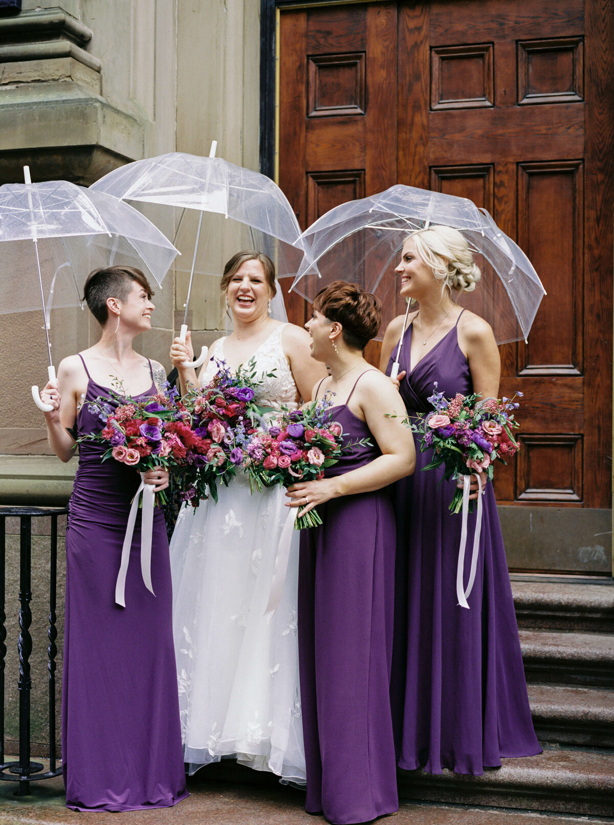 Bride with bridesmaids wearing purple dresses and umbrellas standing outside the Halifax Club in Nova Scotia