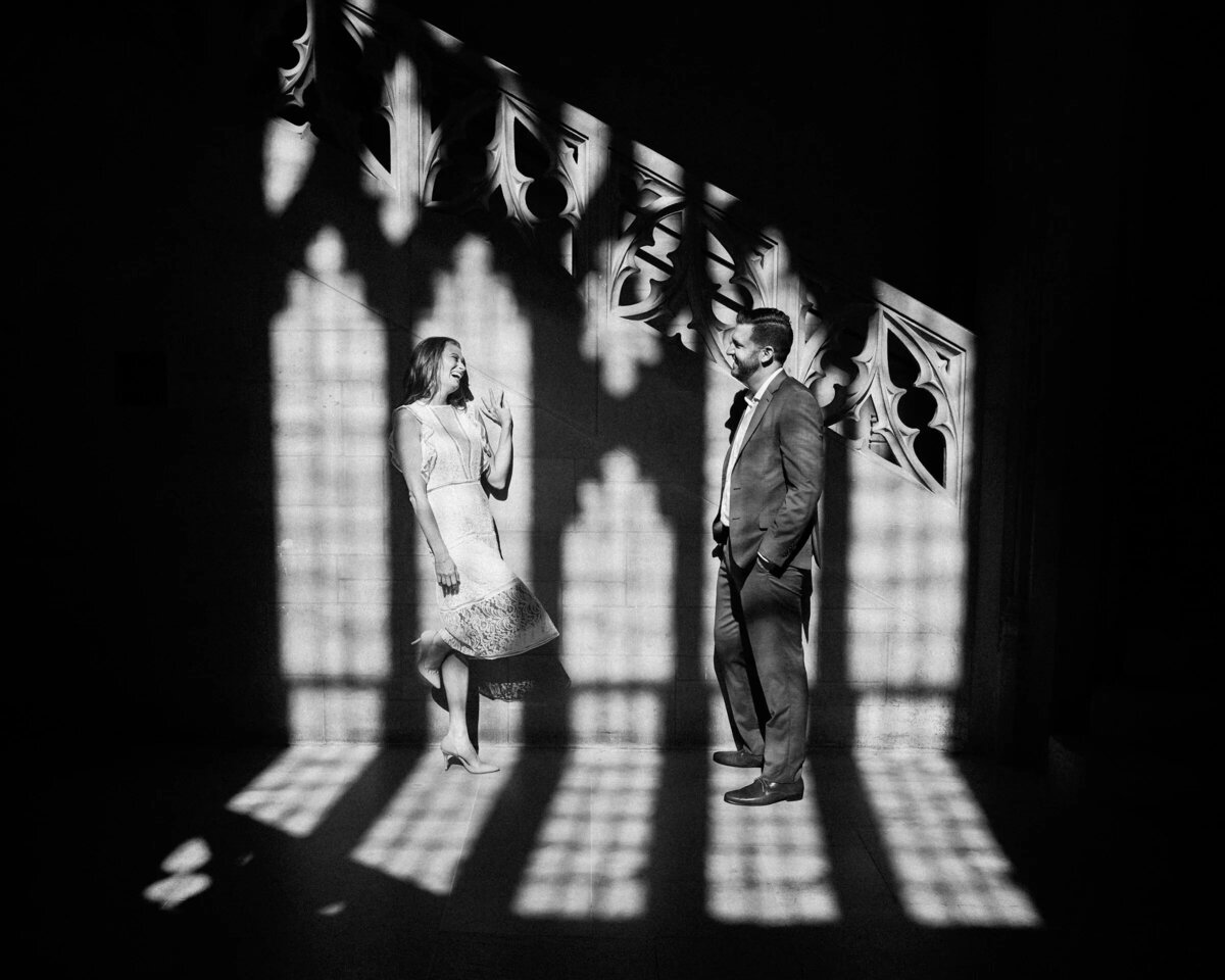 Black and white photo of a couple standing apart, with striking shadows of window panes and leaves cast upon them