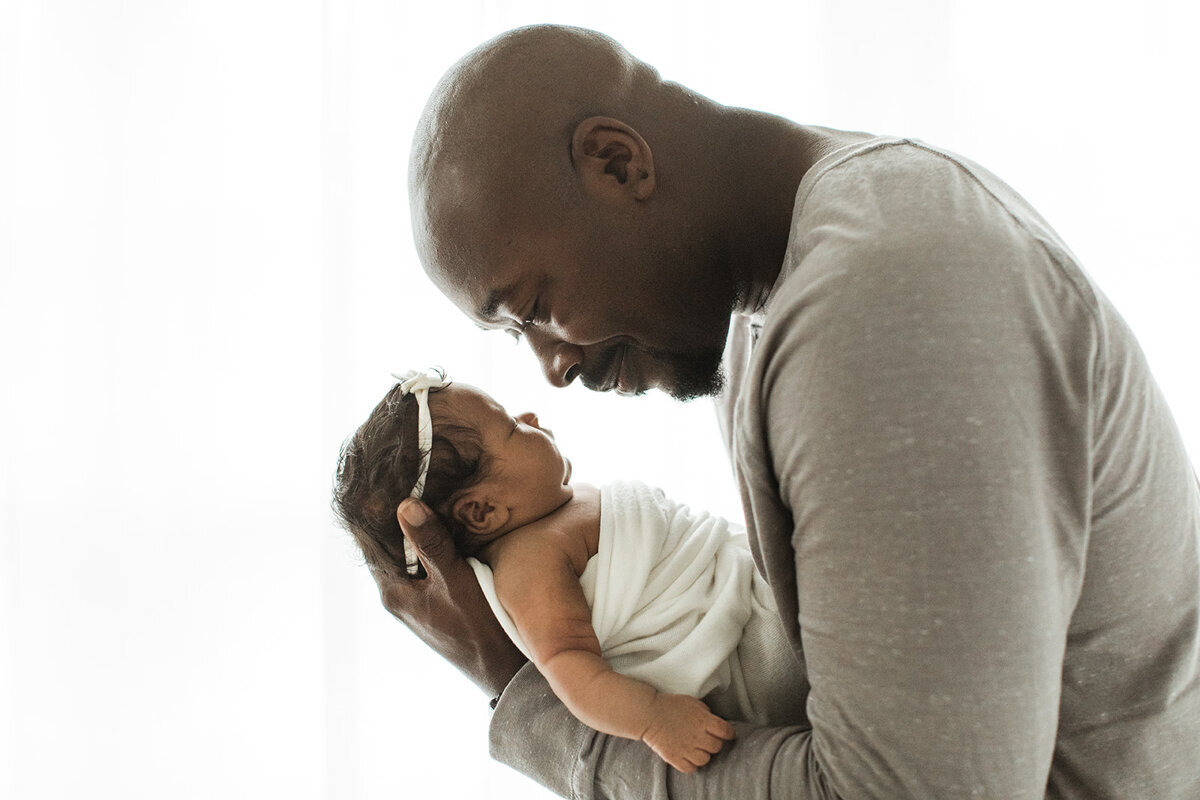 Black father gently holds his newborn daughter and smiles