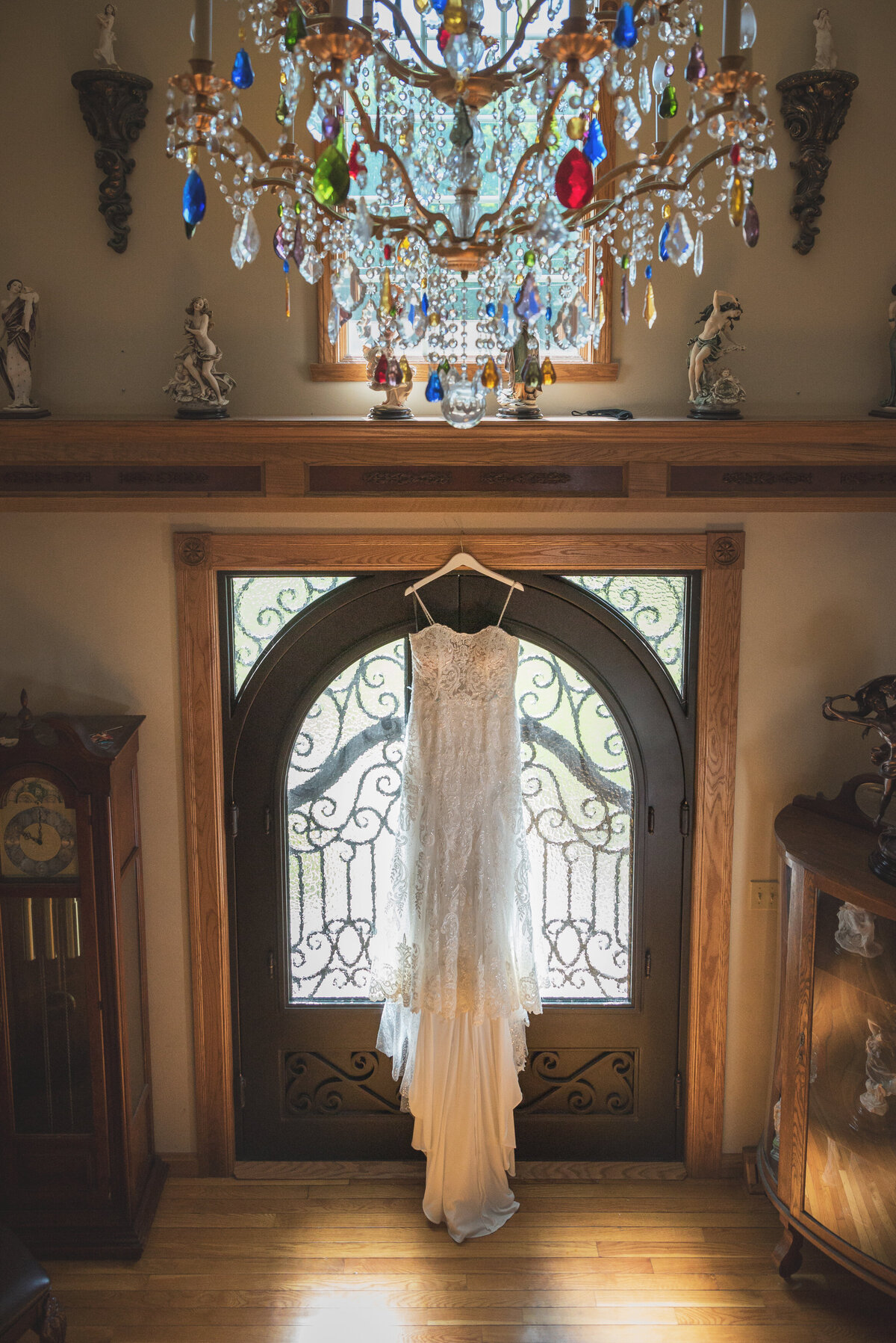 Wedding dress hanging below colorful chandelier.