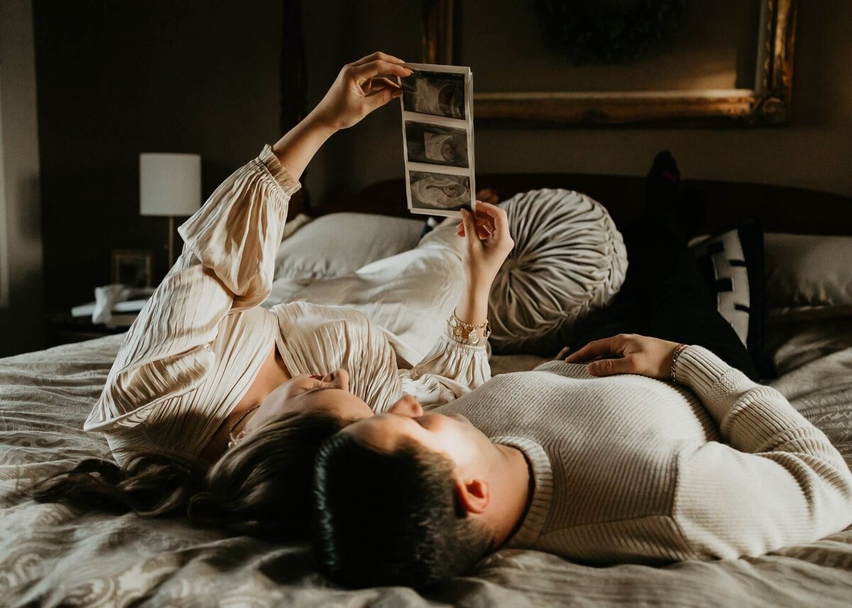 A couple laying on a bed holding a photo of their baby, taken by a Pittsburgh maternity photographer.