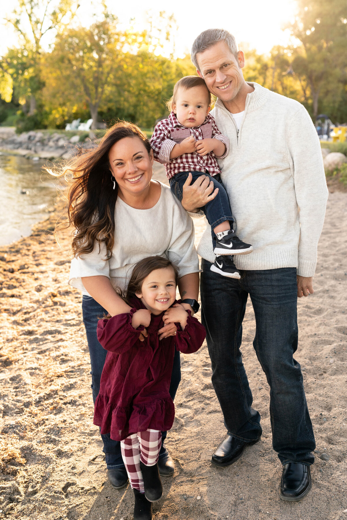 Family of parents and little boy and girl smile on the beach at sunset.