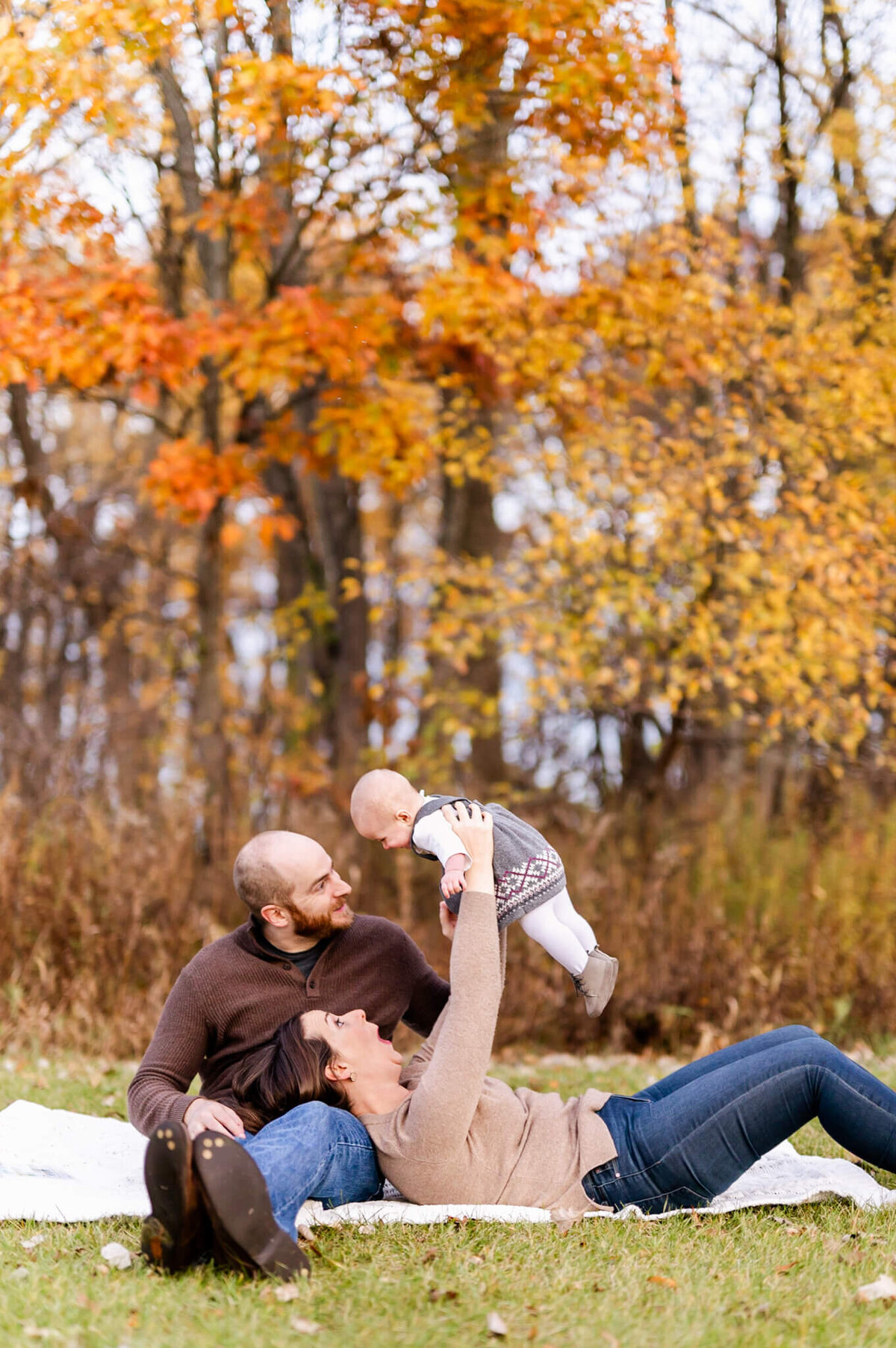 Mom laying on dad raising toddler in the air during a Chicago photo session with Everything is Grace.