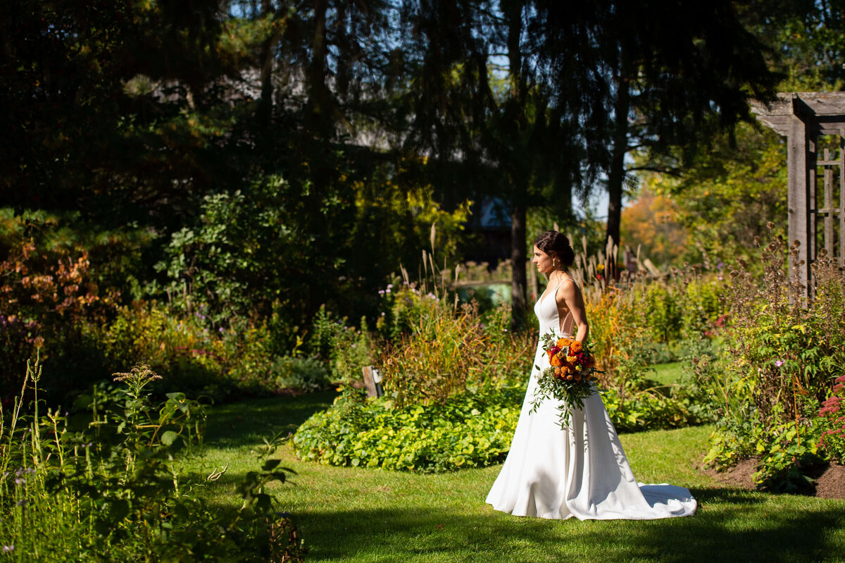 Bride waiting for first looks in the garden at Strathmere wedding venue holding a fall bouquet in her hand
