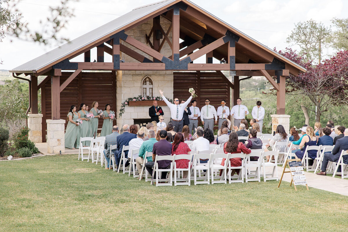 flower man cheers at end of aisle at outdoor  ceremony Milestone New Braunfels Texas rustic wedding