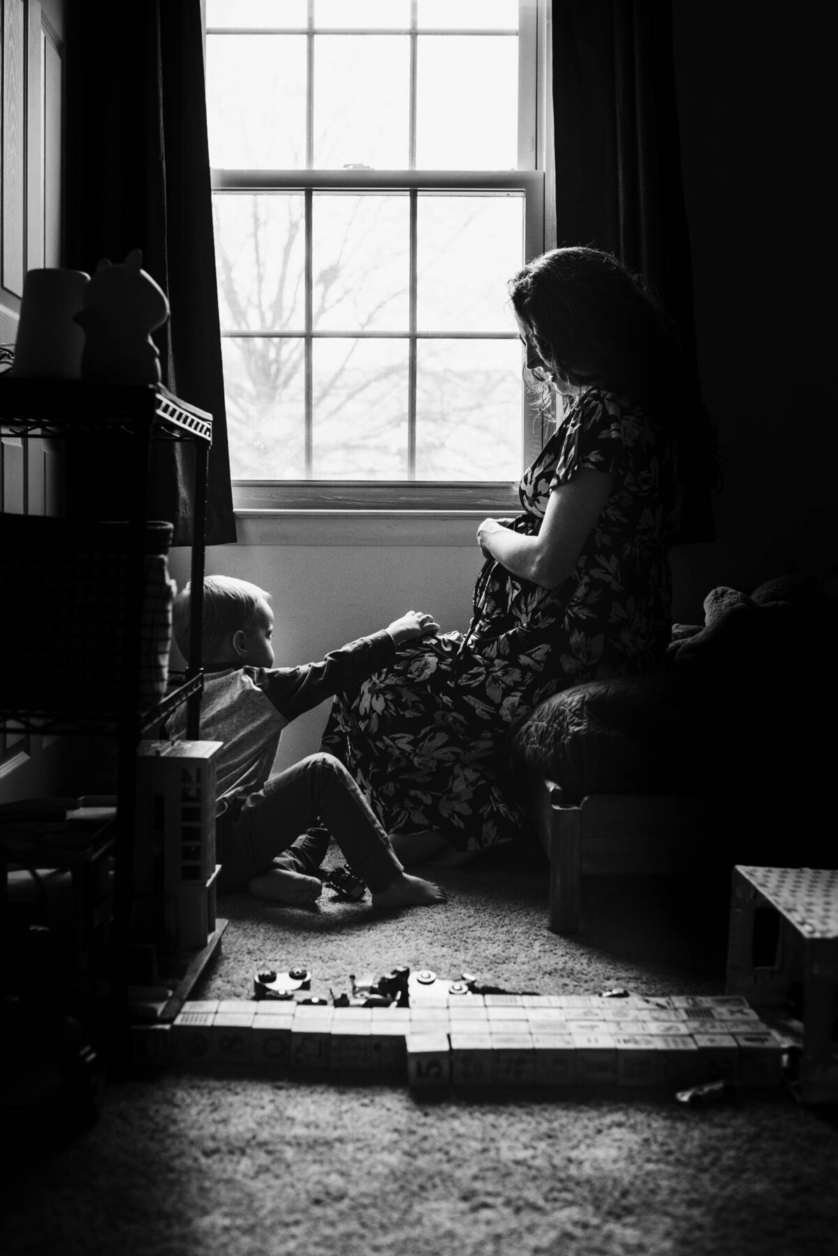 Indoor Black and White kids playing with toys while Mom sits on bed holding pregnant belly