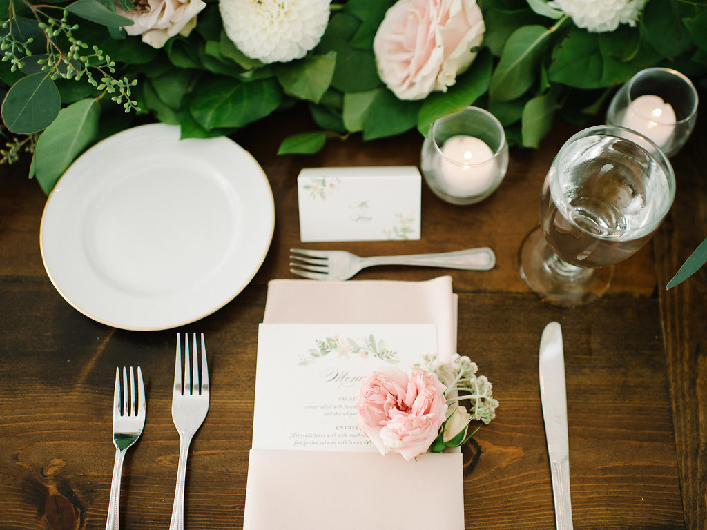 Dinner place setting with blush garden rose napkin flower accent.