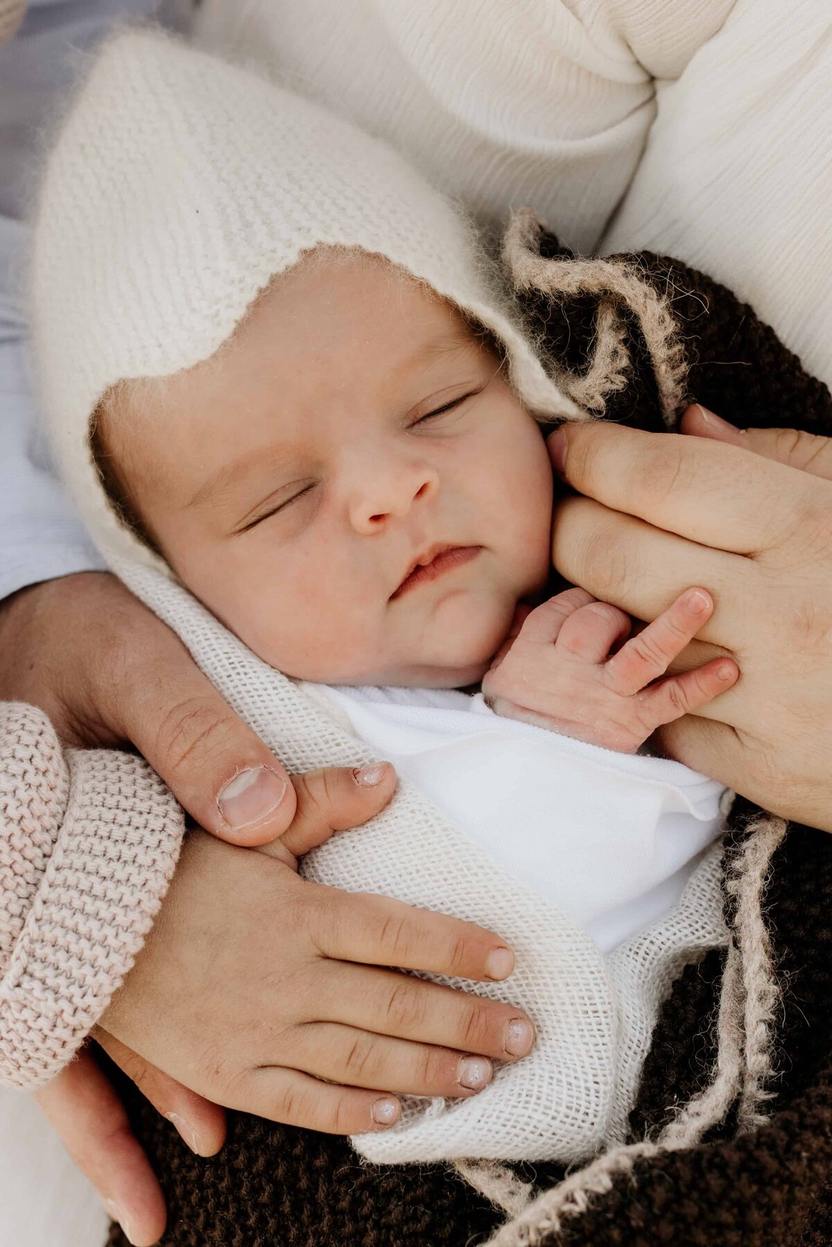 Ansikt til en nyfødt jente med lue som sover i  armene til familie sin.