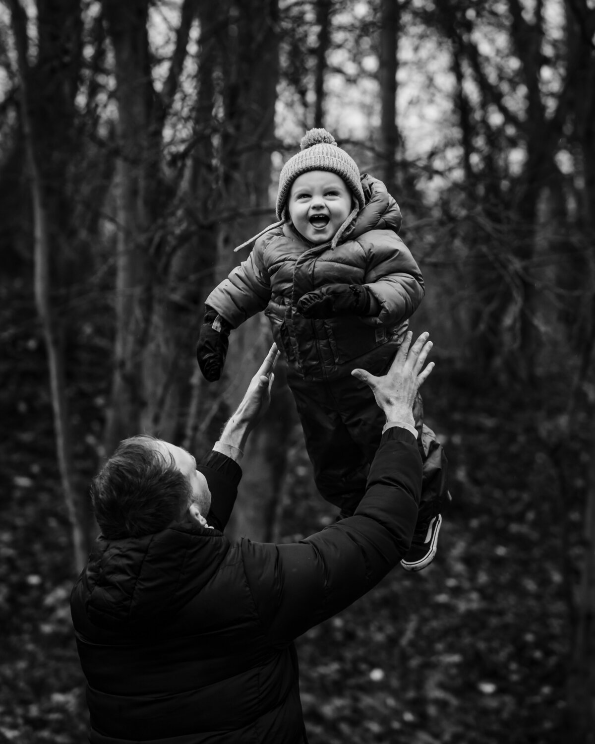 black and white image of dad throwing his son in the air during family photoshoot