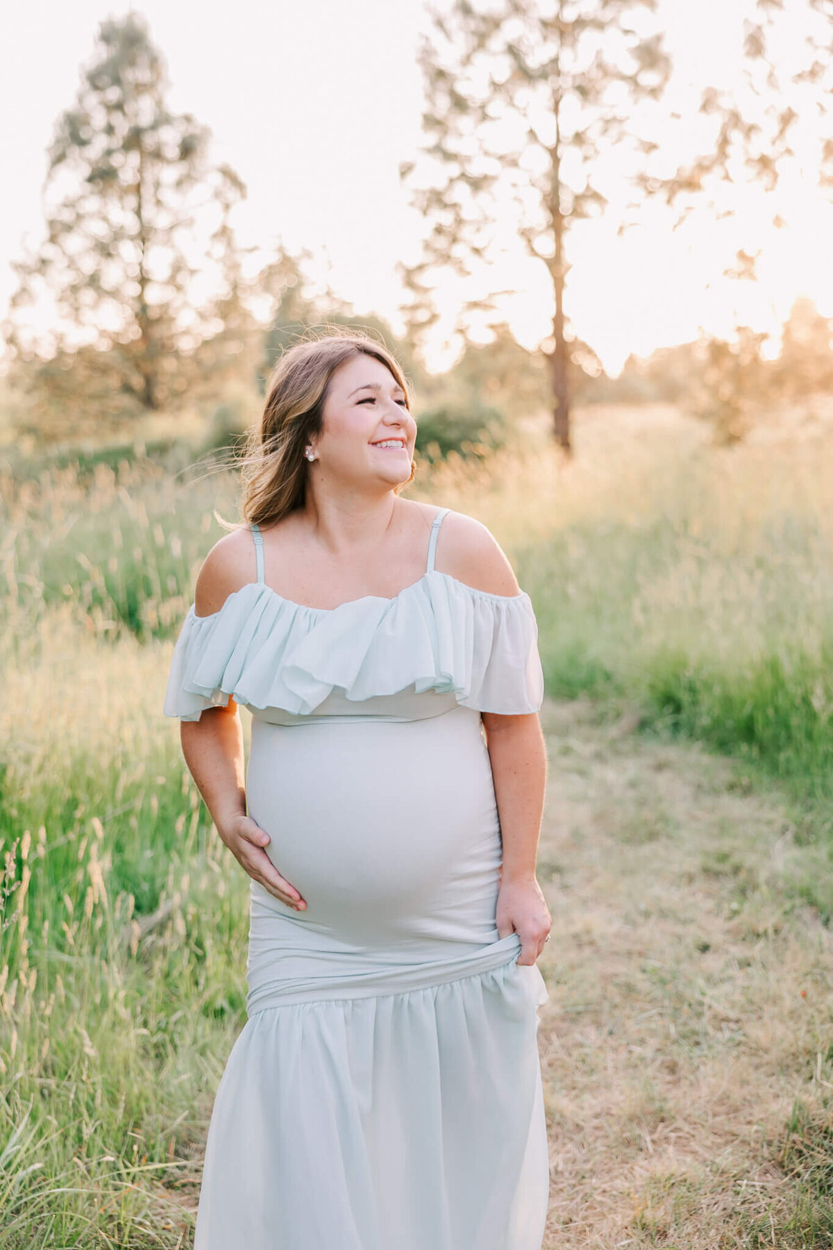 portrait of a pregnant woman taken by ann marshall photography in portland oregon. She is walking and smiling with her hand on her belly wearing a green dress.
