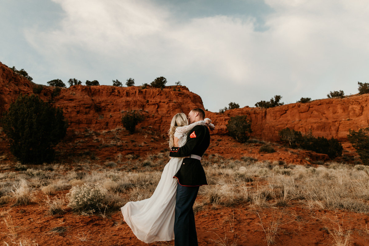 groom holding and kissing wife in the desert