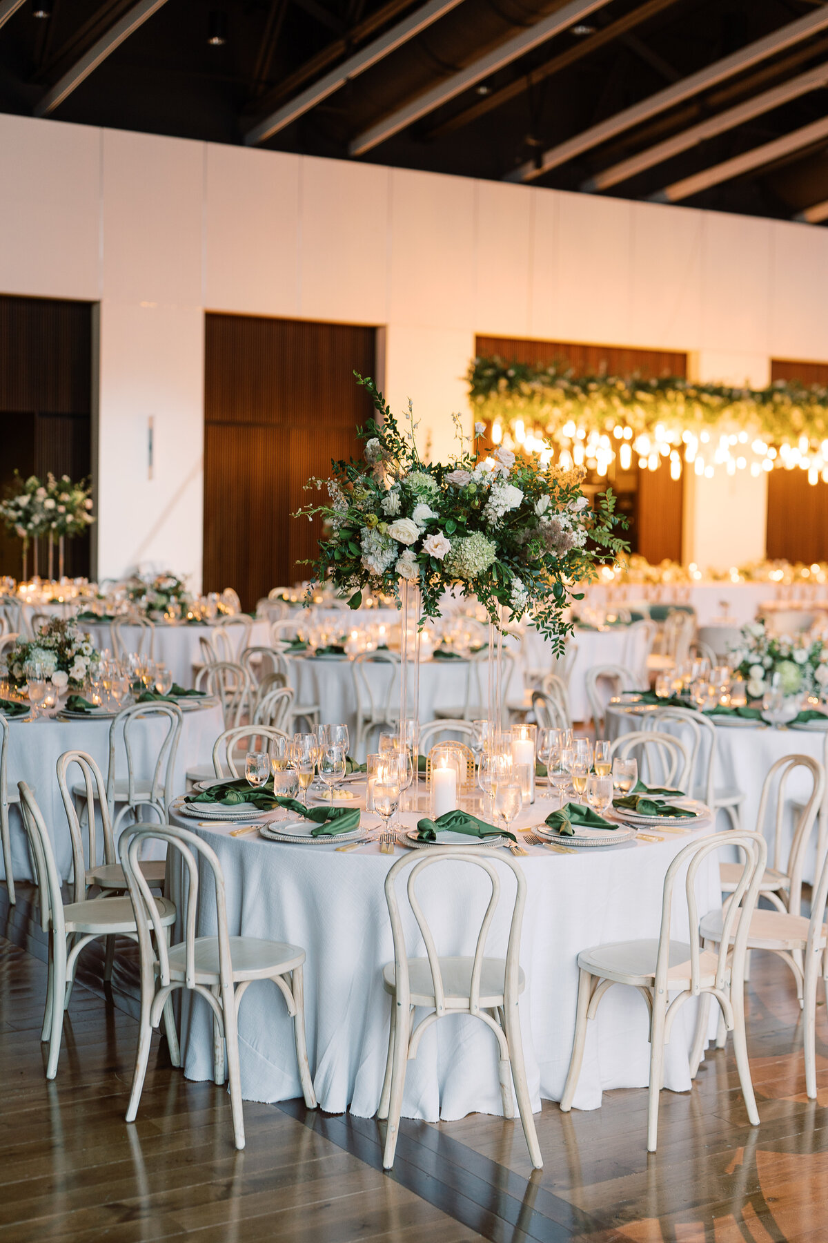 Elevated floral centerpieces for garden-inspired wedding in downtown Nashville. Classic white and green wedding with floral colors in cream, white, taupe, and champagne. Timeless pillar and votive candles in white accent this lush tall floral design. Design by Rosemary & Finch in Nashville, TN.