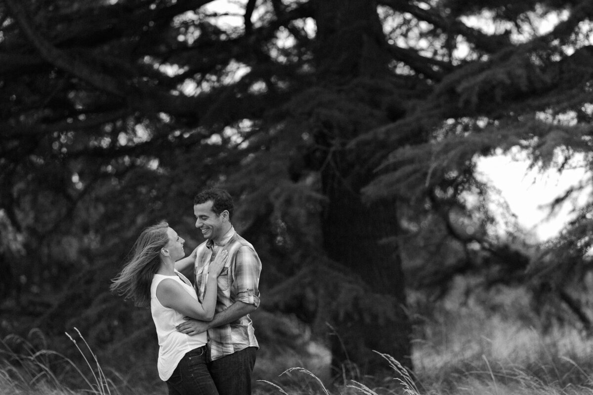Moody and dramatic engagement session in field at Discovery Park in Seattle happy couple laughing under tree candid photo by Joanna Monger Photography