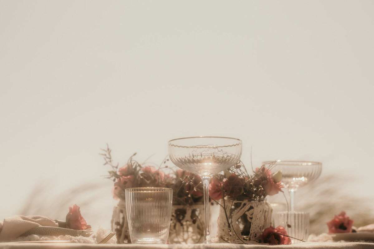 Im Fokus steht ein Champagnerkelch, der vor den rosa Blumen in den Vasen steht.
