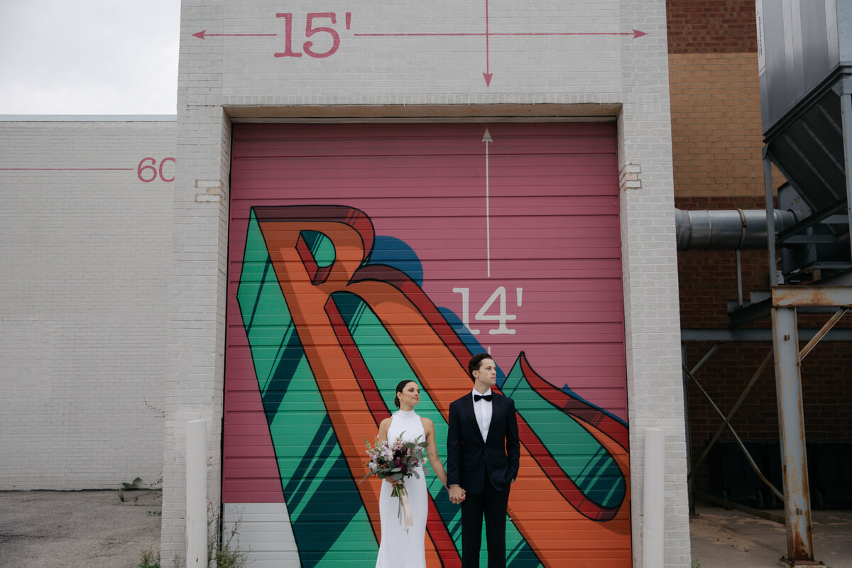 Bride and Groom standing in industrial area in front of painted mural