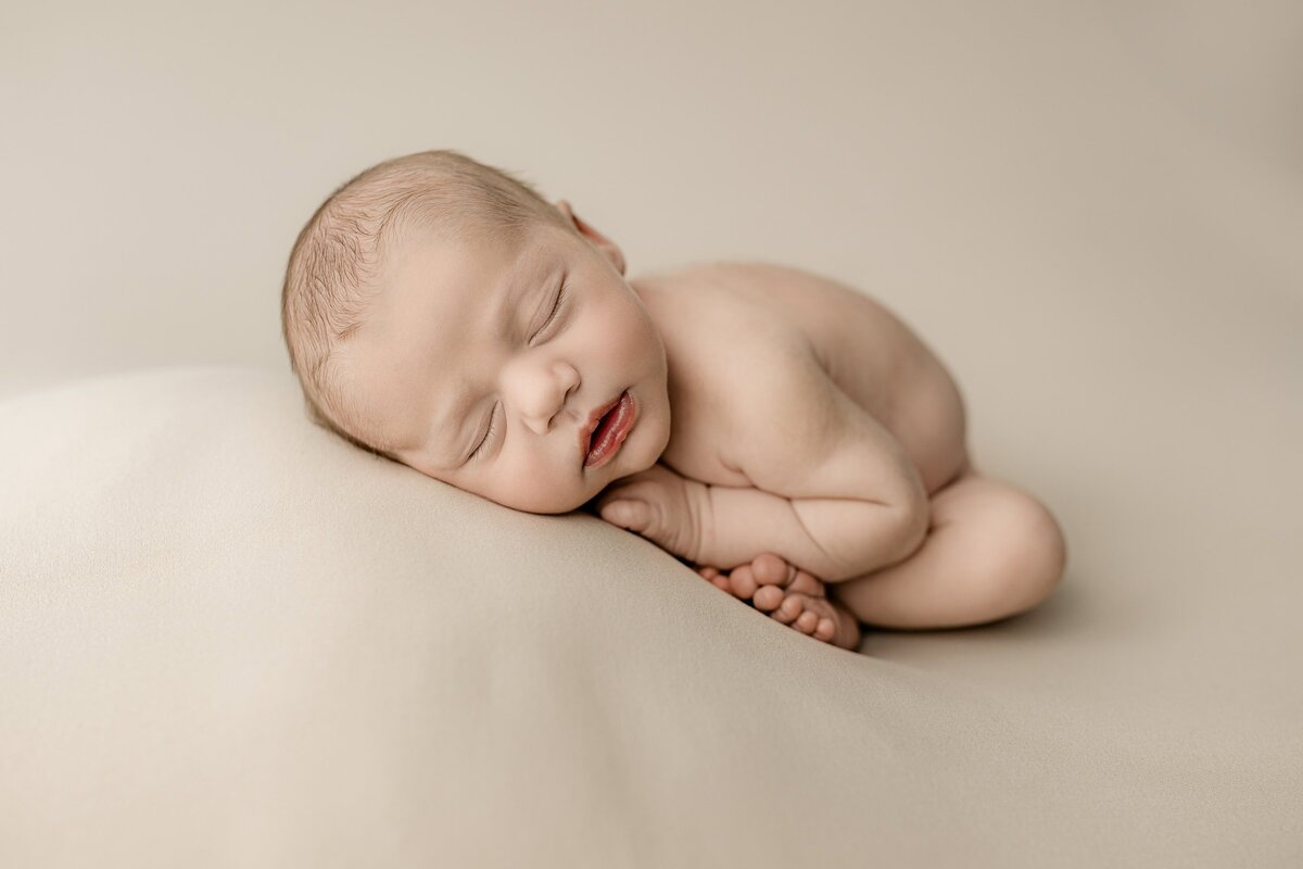 newborn baby boy posed in womb pose naked laying on neutral drop