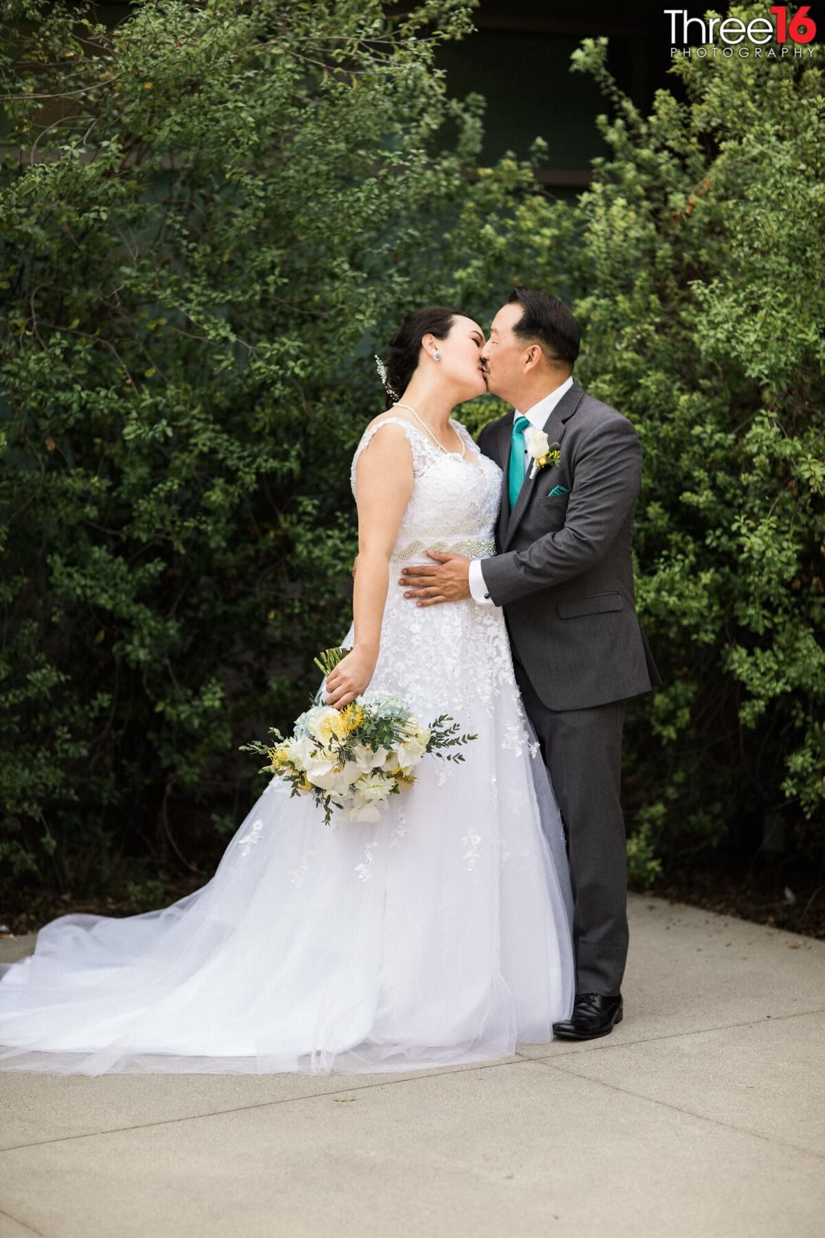 Bride and Groom share a kiss in front of green plants at the Fullerton Community Center wedding venue