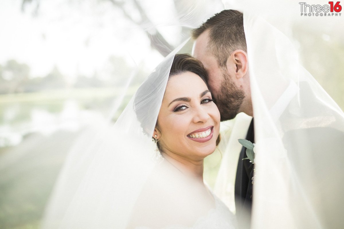 Groom whispers into his Bride's ear as she smiles for the camera with both of them under her veil