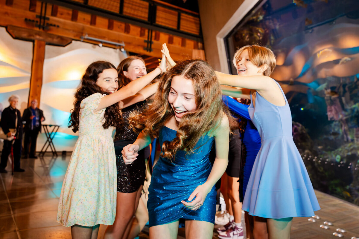 A laughing girl in a blue dress enters her party from under her firends arms