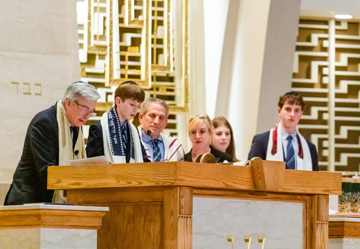 A teen boy at the bimah reads from the torah with the rabbi and family looking on for some Bellevue Bar and Bat Mitzvah Photography