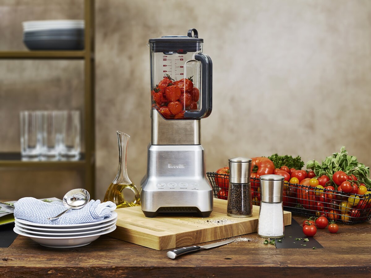 A blender on a cutting board filled with strawberries.