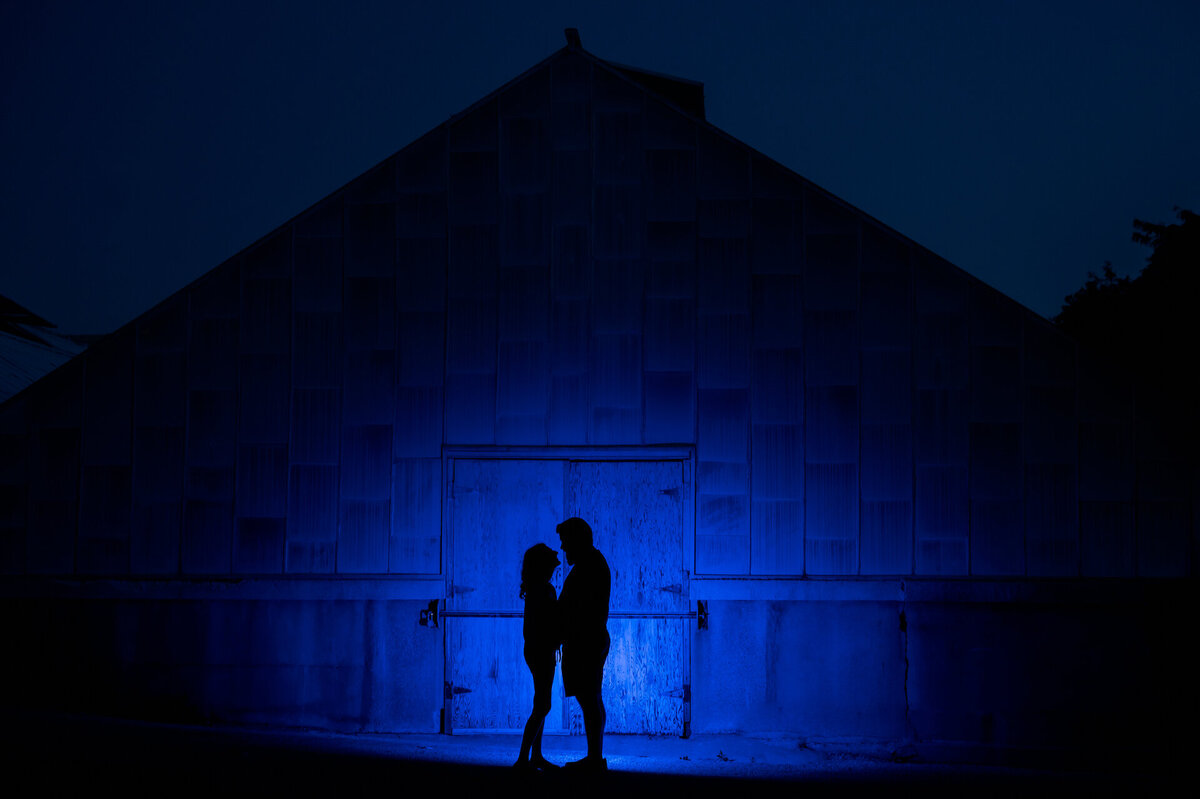 A couple is Silhouetted in front of a blue barn