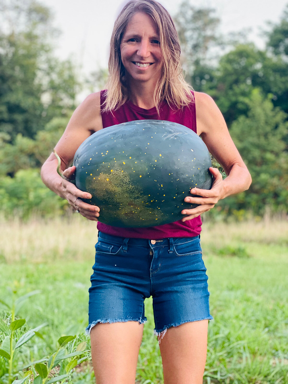 Aime an elopement photographer holding a giant watermelon she grew in her garden