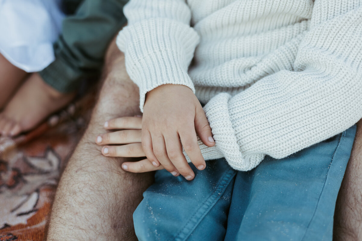 Portrait of little boys hands on his dad's lap.