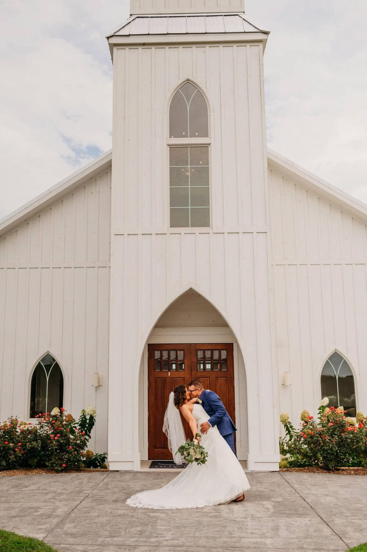 photo of a bride and groom dipping and kissing in front of a white wedding chapel in Tennessee