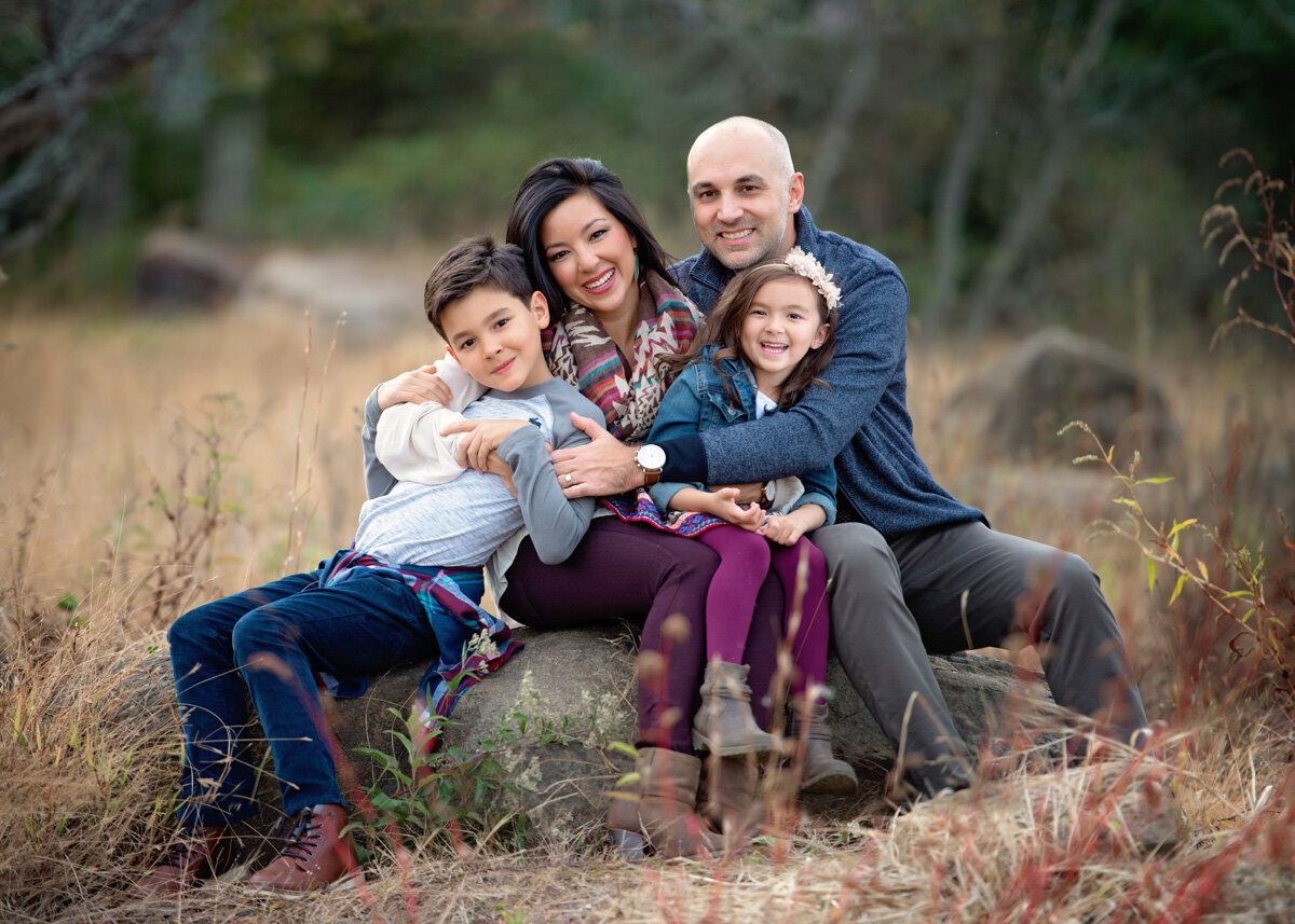 Family session located outside with family sitting on a boulder