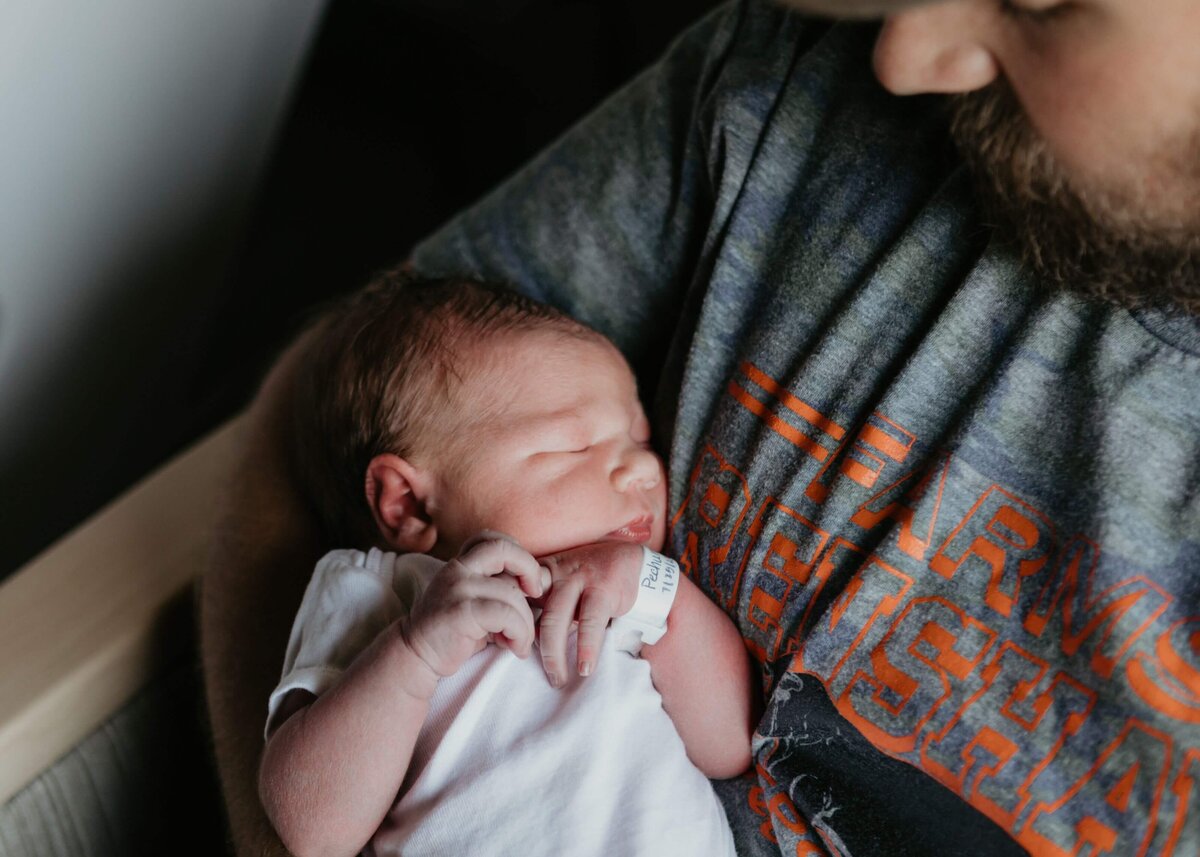 A man holding a baby in his arms posing for a Pittsburgh newborn photographer.