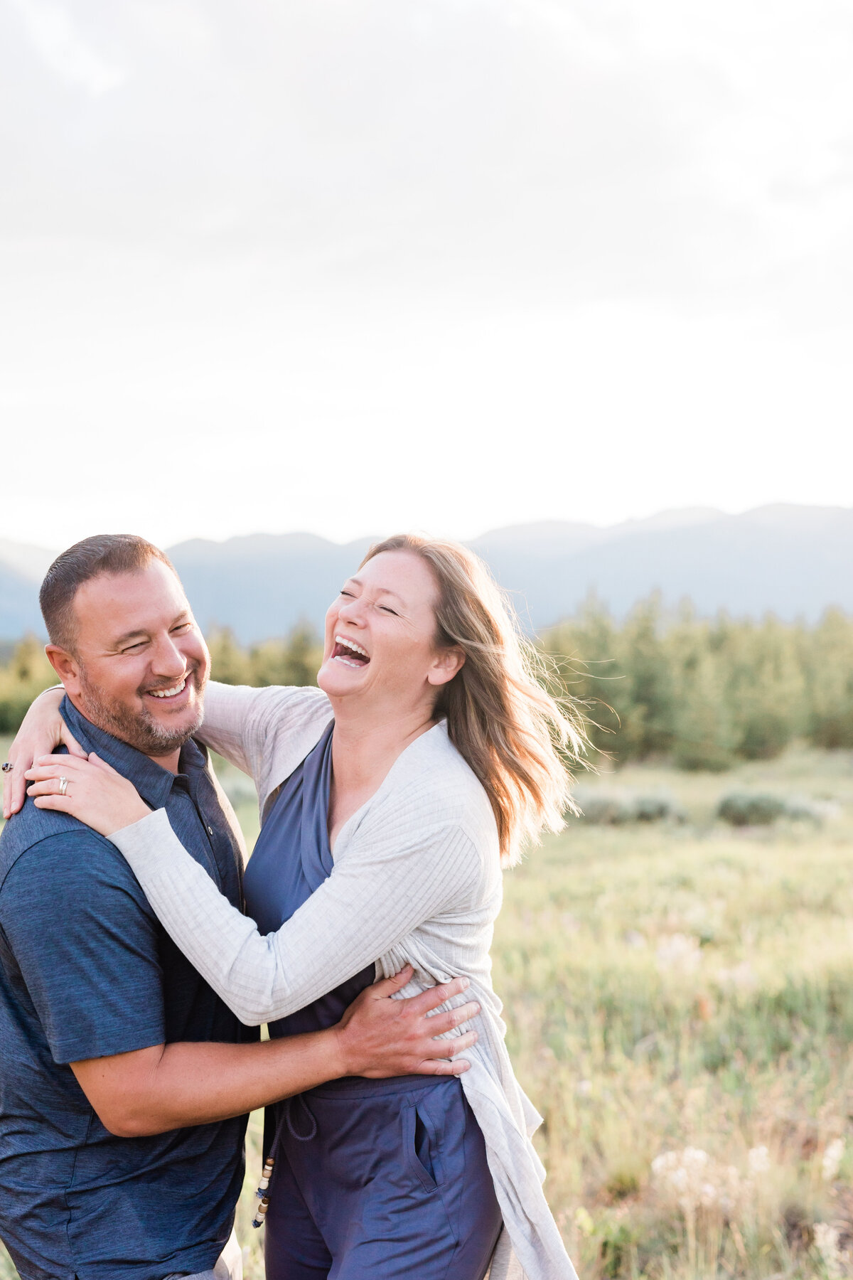 A husband and wife are laughing with one another on a warm summer night in a field on Swan Mountain