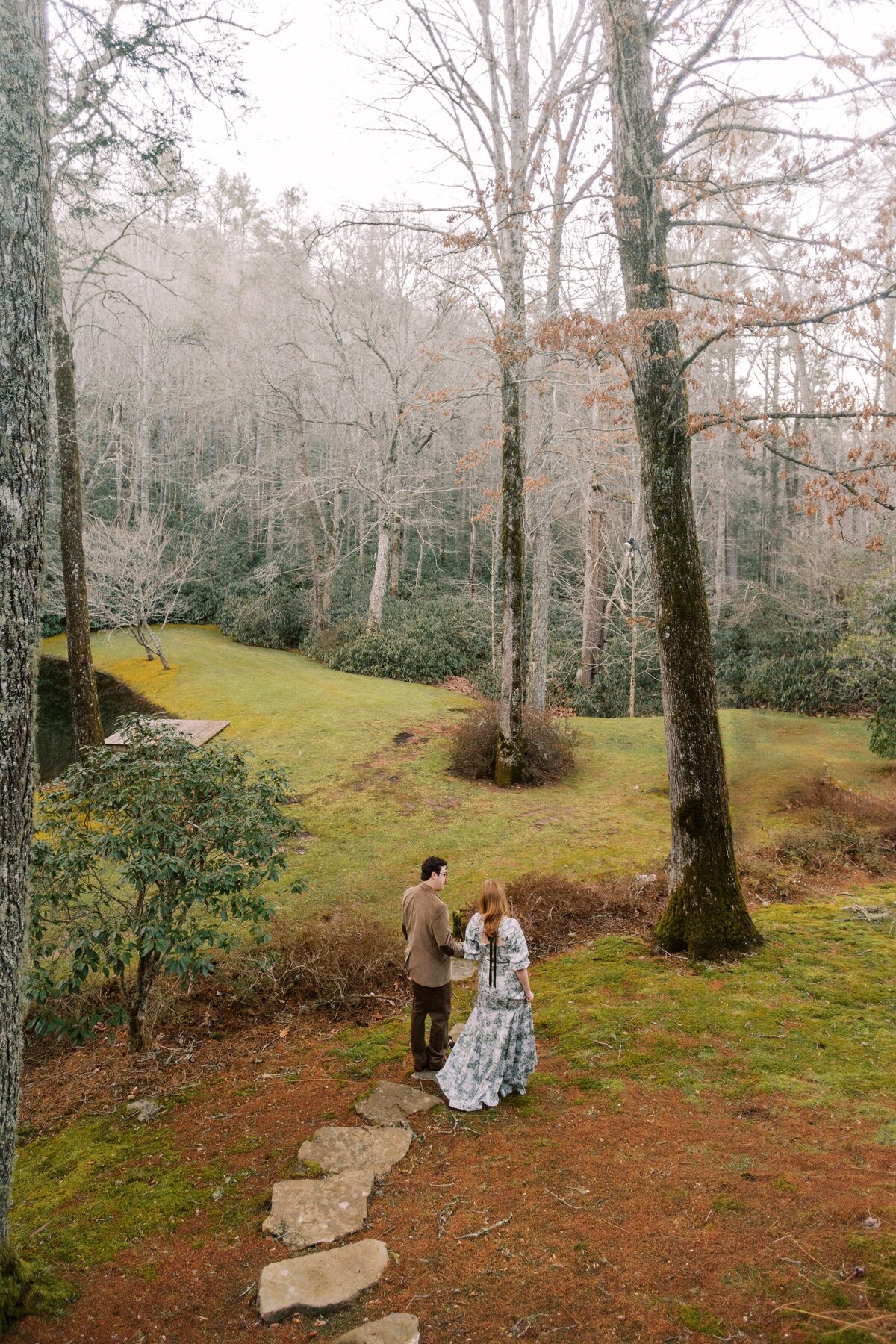 engaged couple walk together through a wooded area
