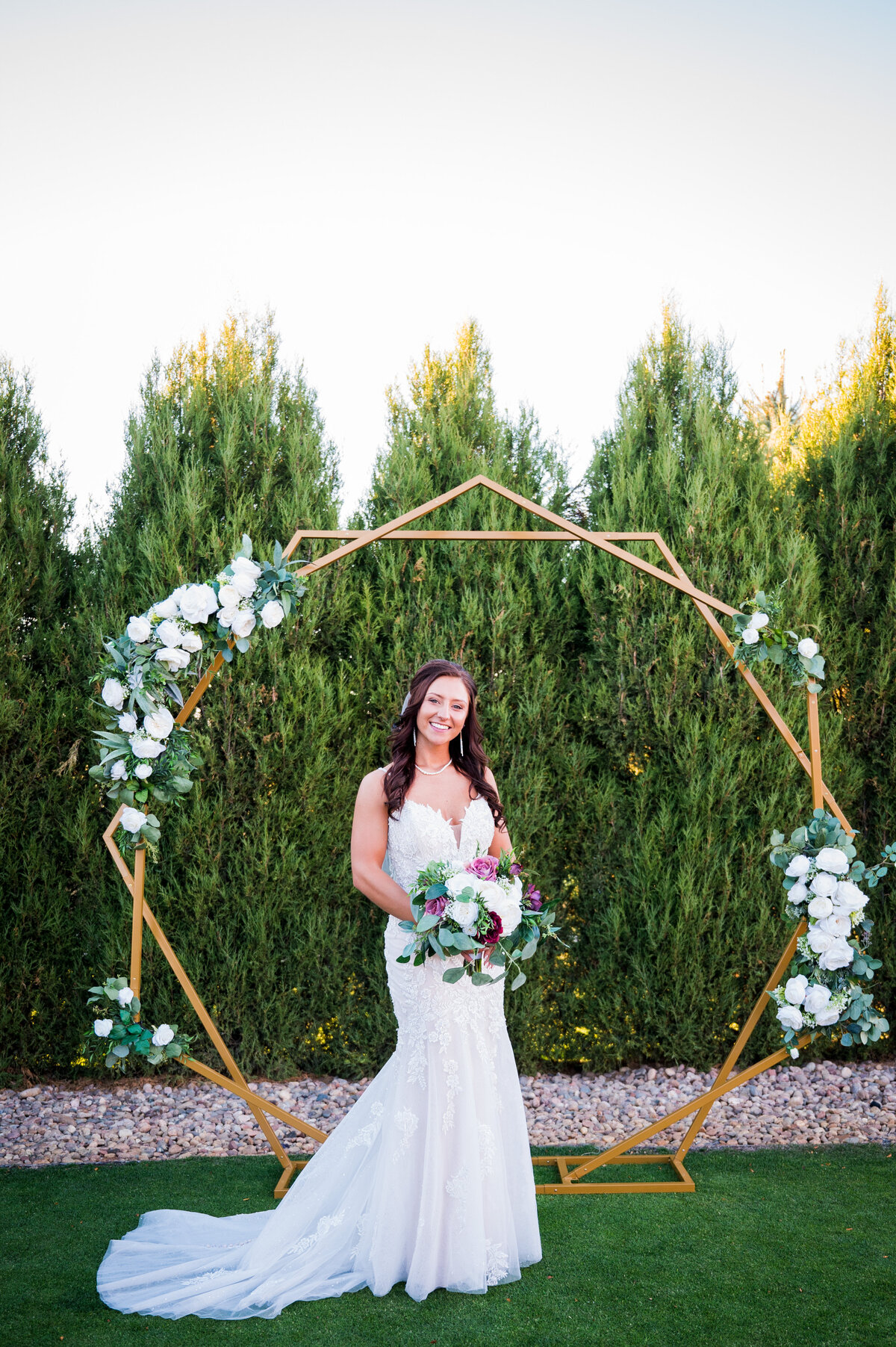 A bride smiles at the camera, standing in front of her wedding arch and her Colorado wedding venue.
