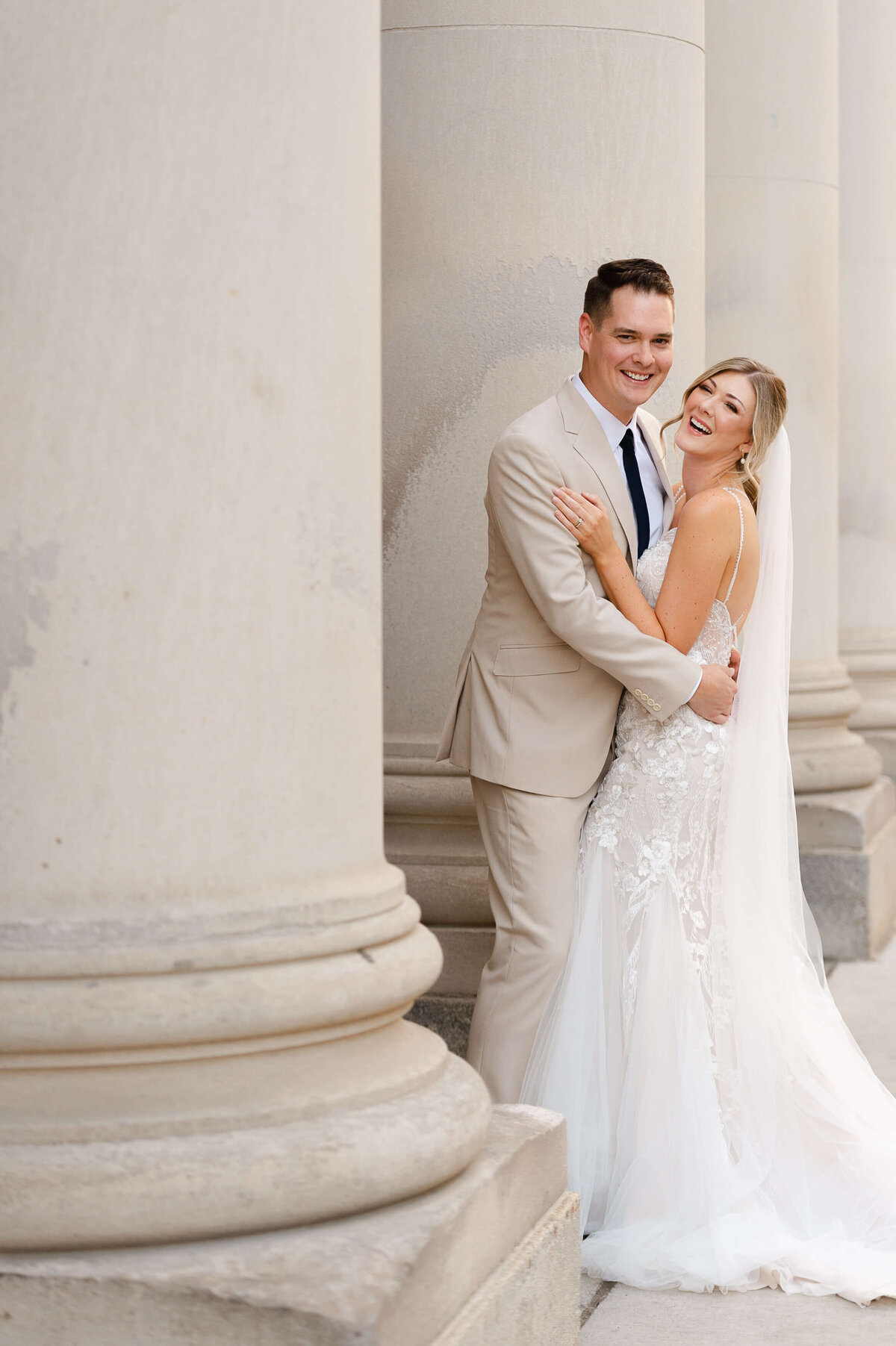 a full length photo of a bride and groom laughing and smiling together amongst the columns of the Chateau Laurier venue taken by Ottawa wedding photographer JEMMAN Photography