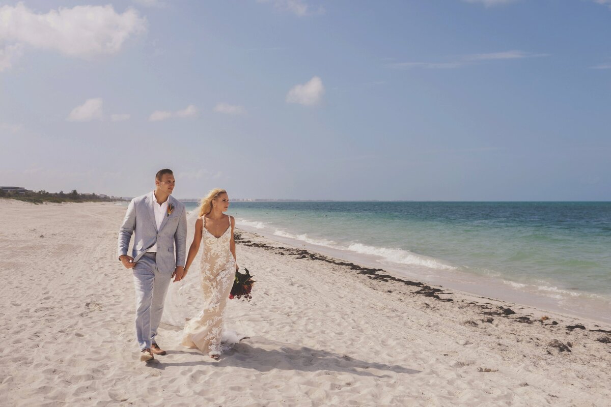 Bride and groom walking down beach holding hands in Cancun