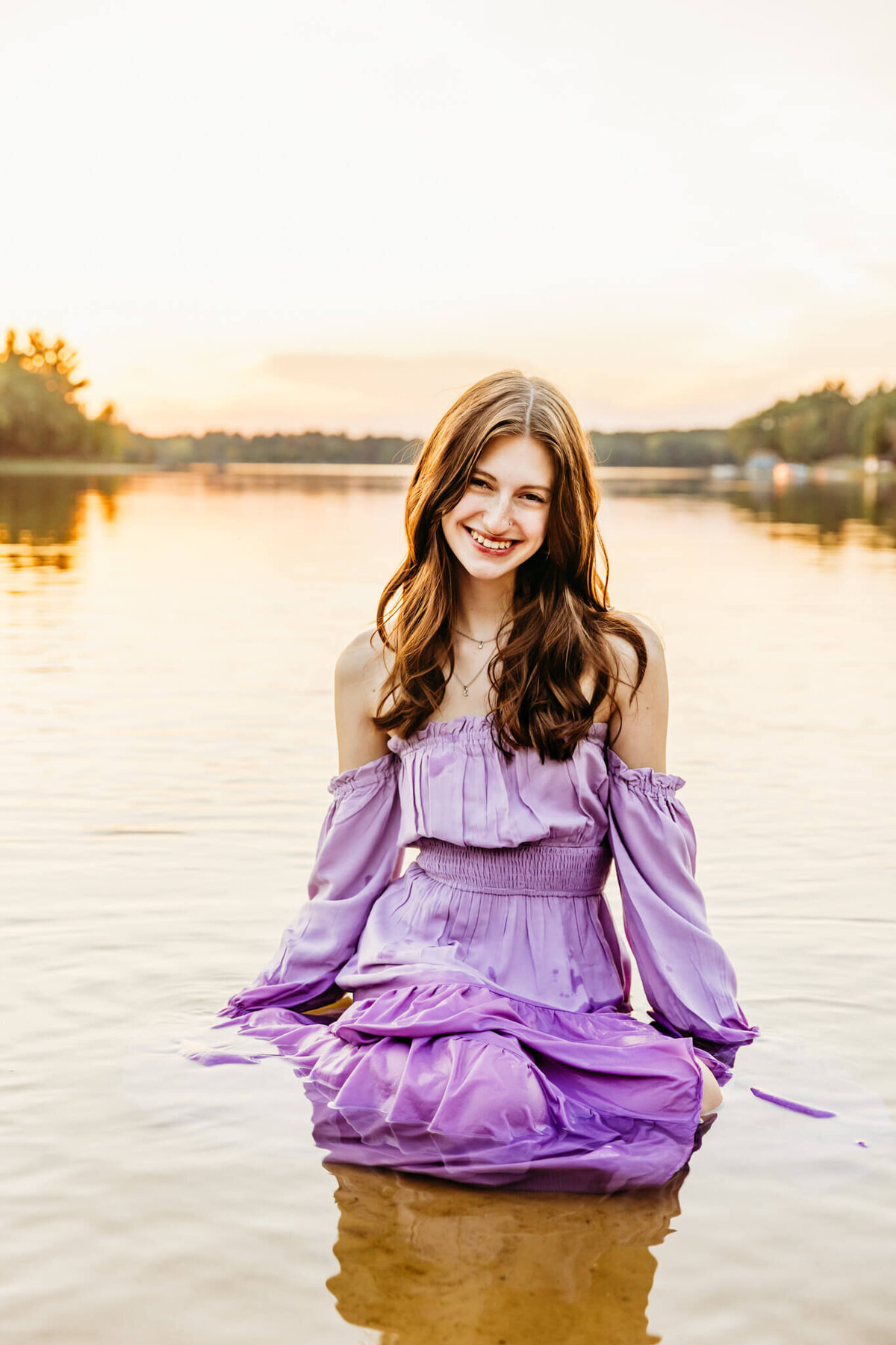 pretty teen girl sitting in a purple gown in the lake during senior photography session