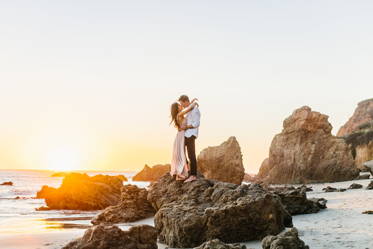 Engagement session photo at the beach on a rock at sunset