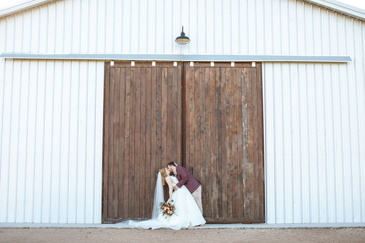 bride and groom kiss in front of large barn doors at Allen Farmhaus in New Braunfels