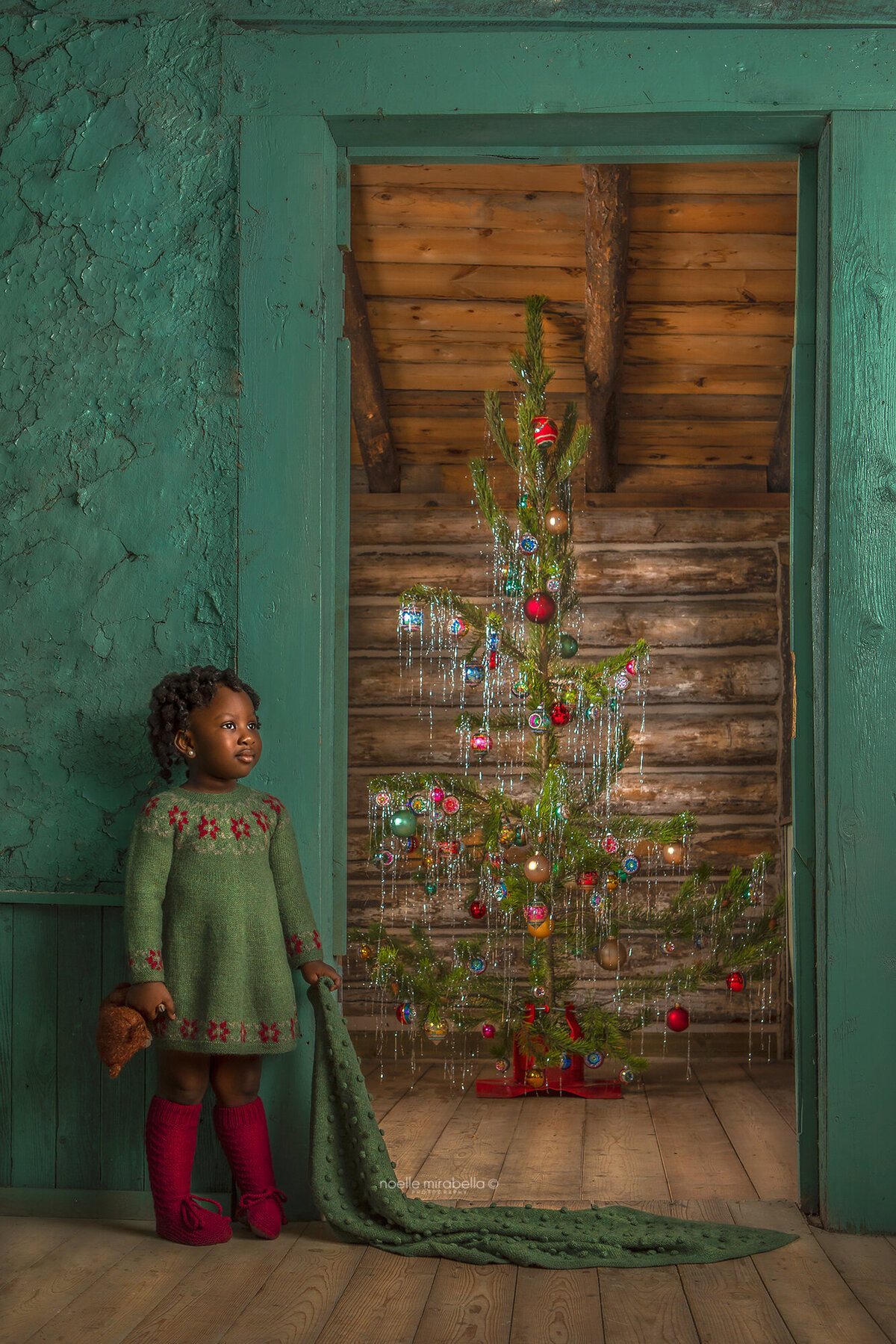 Young girl standing in doorway with vintage style pine Christmas tree in the background.