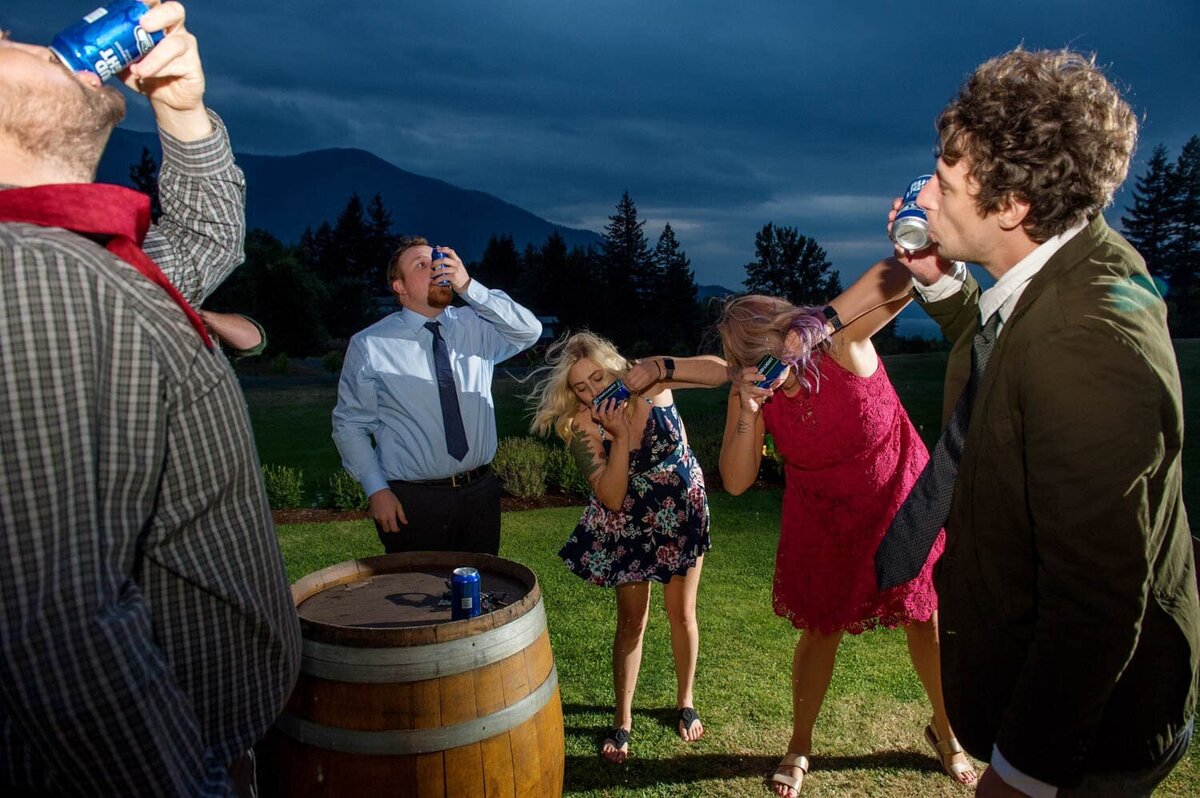 wedding guests shotgun beer during the reception as the sun sets