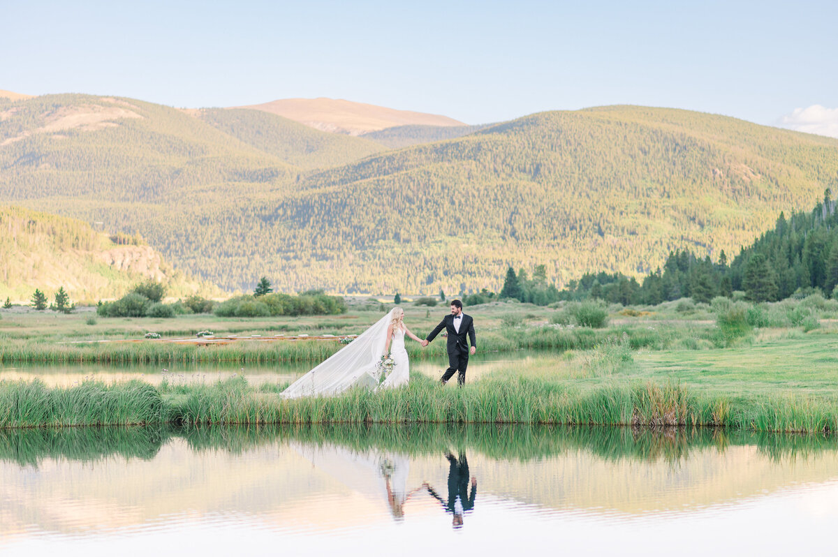 A groom and bride walking along a lake at sunset at Camp Hale near Vail, Colorado.