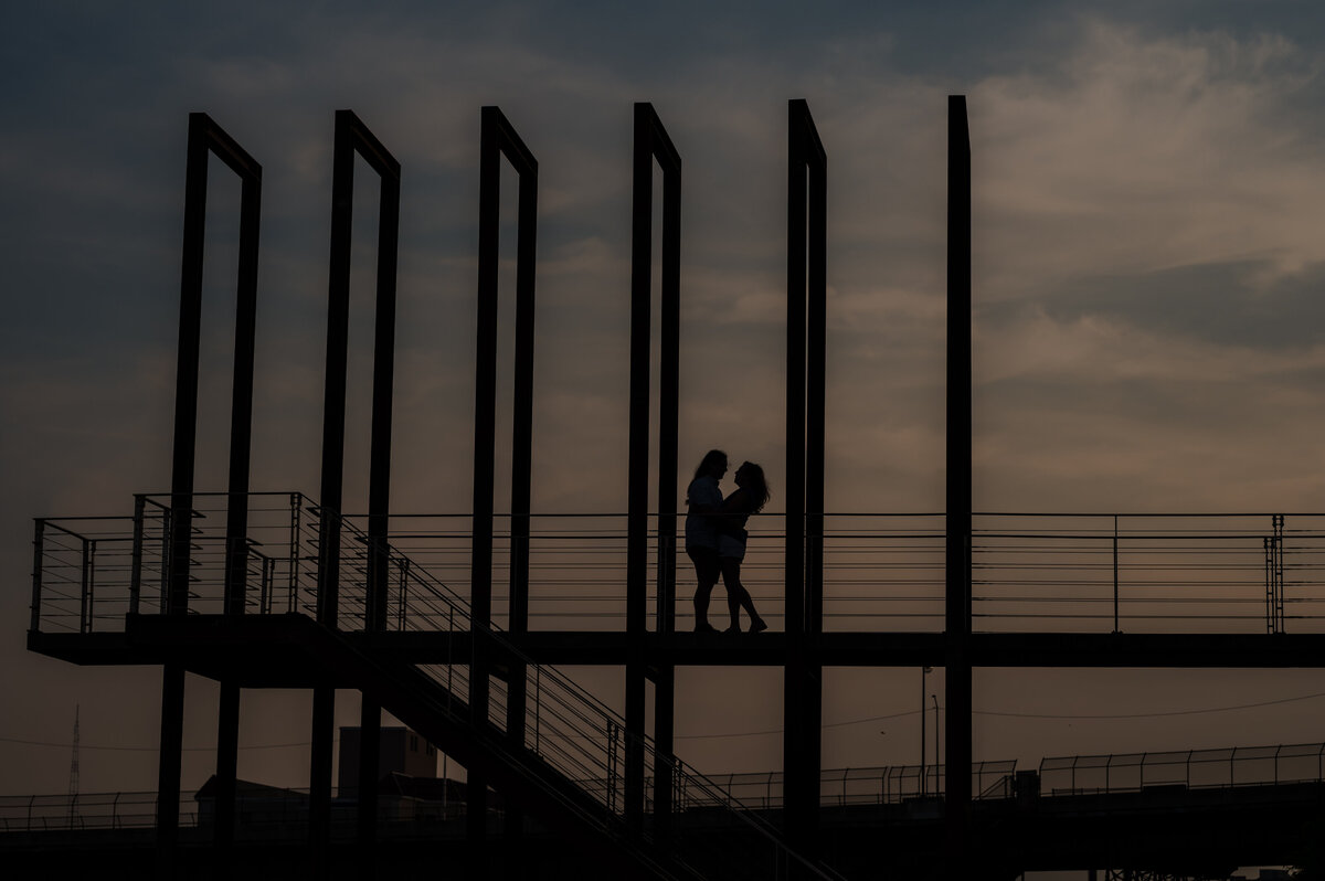 A couple stands on a bridge surrounded by sky