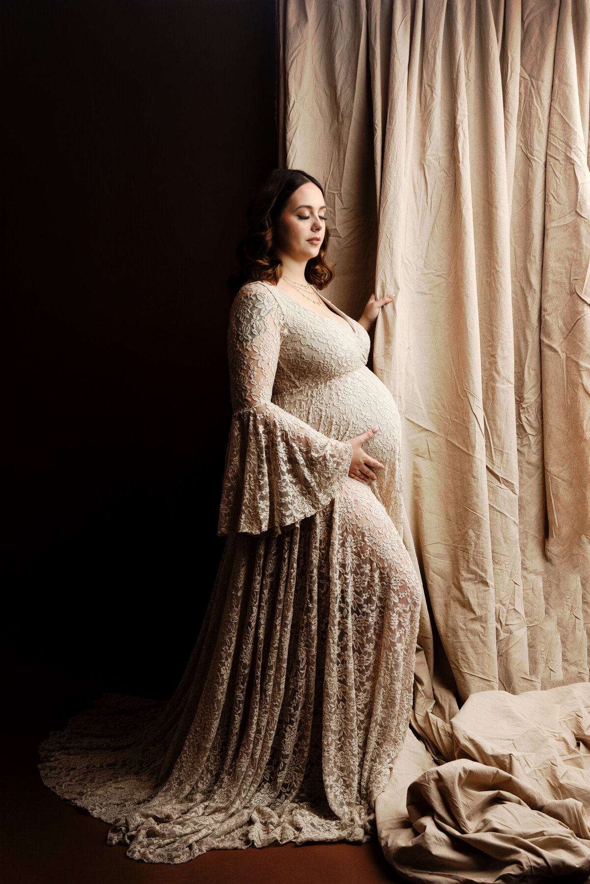 st-louis-maternity-photographer-mom-in-tan-lace-gown-standing-with-muslin-fabric-and-brown-backdrop