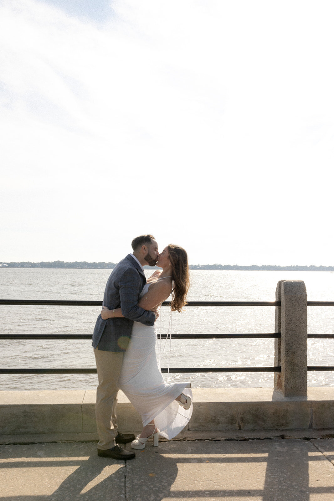Couple kissing for engagement photo at Charleston battery. Charleston harbor in background